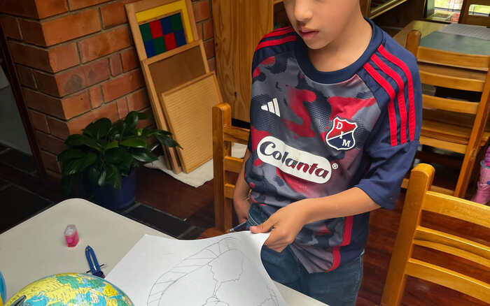 Niño de Taller dibujando los continentes apoyado en un globo terráqueo, trabajo de educación cósmica